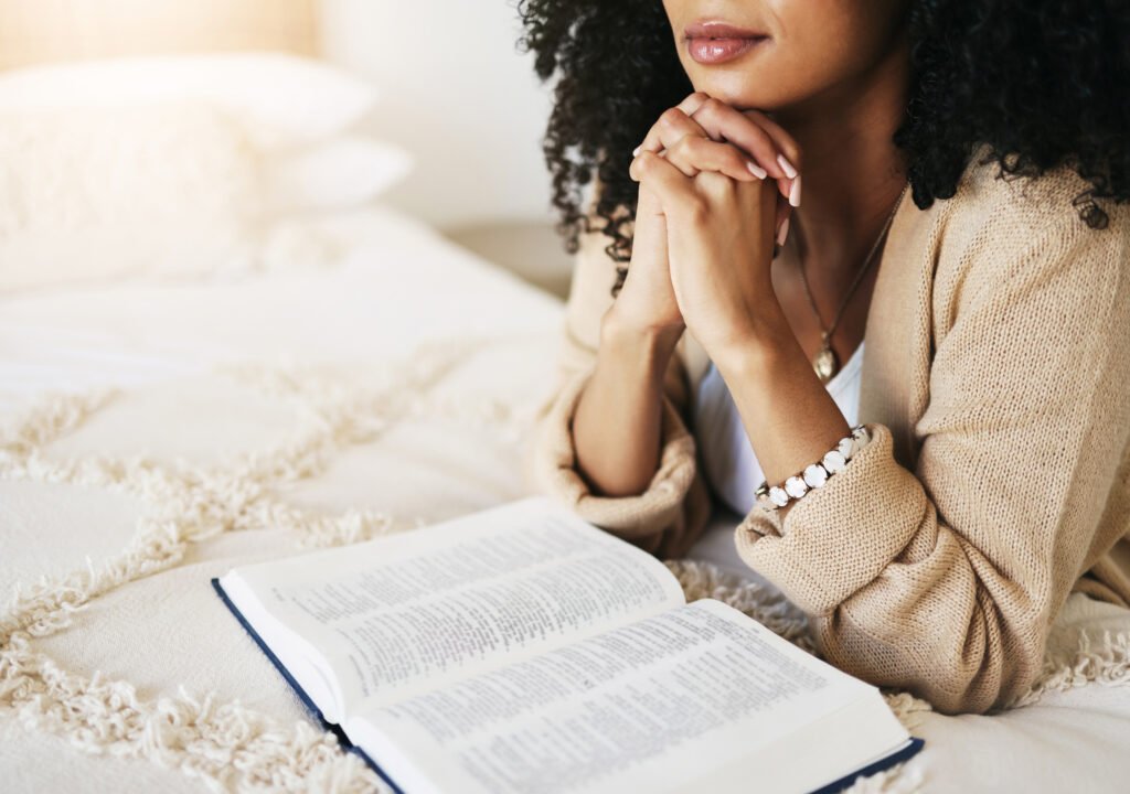 Home bible, prayer and hands praying for hope, religion or help, spiritual or faith in home. god, christian and female or woman worship jesus christ or holy spirit with catholic text or book for peace.
